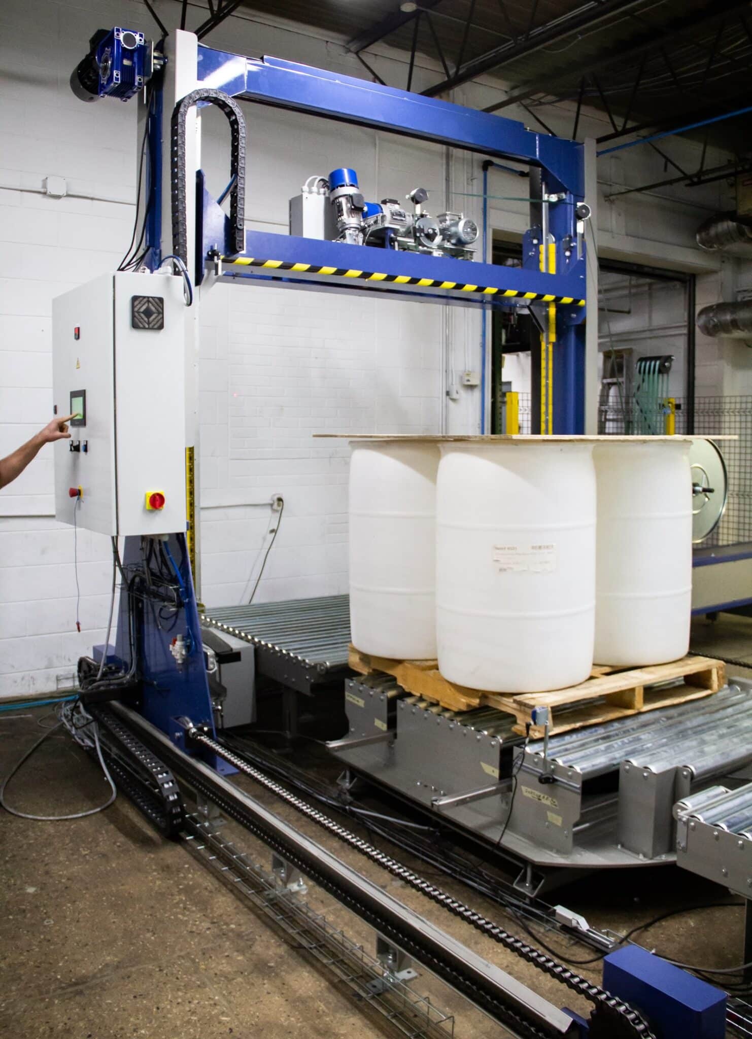 A blue Handle It vertical pallet strapper about to wrap four white 55-gallon drums.